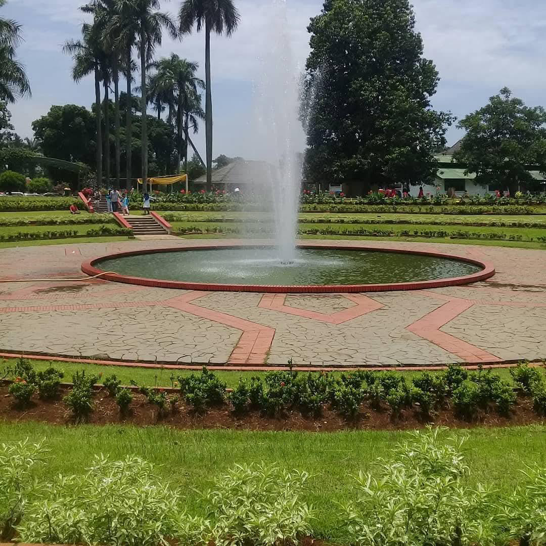 A circular fountain in the Bogor botanical garden, ringed by red brick paths and clipped hedges, palms rising in the background.